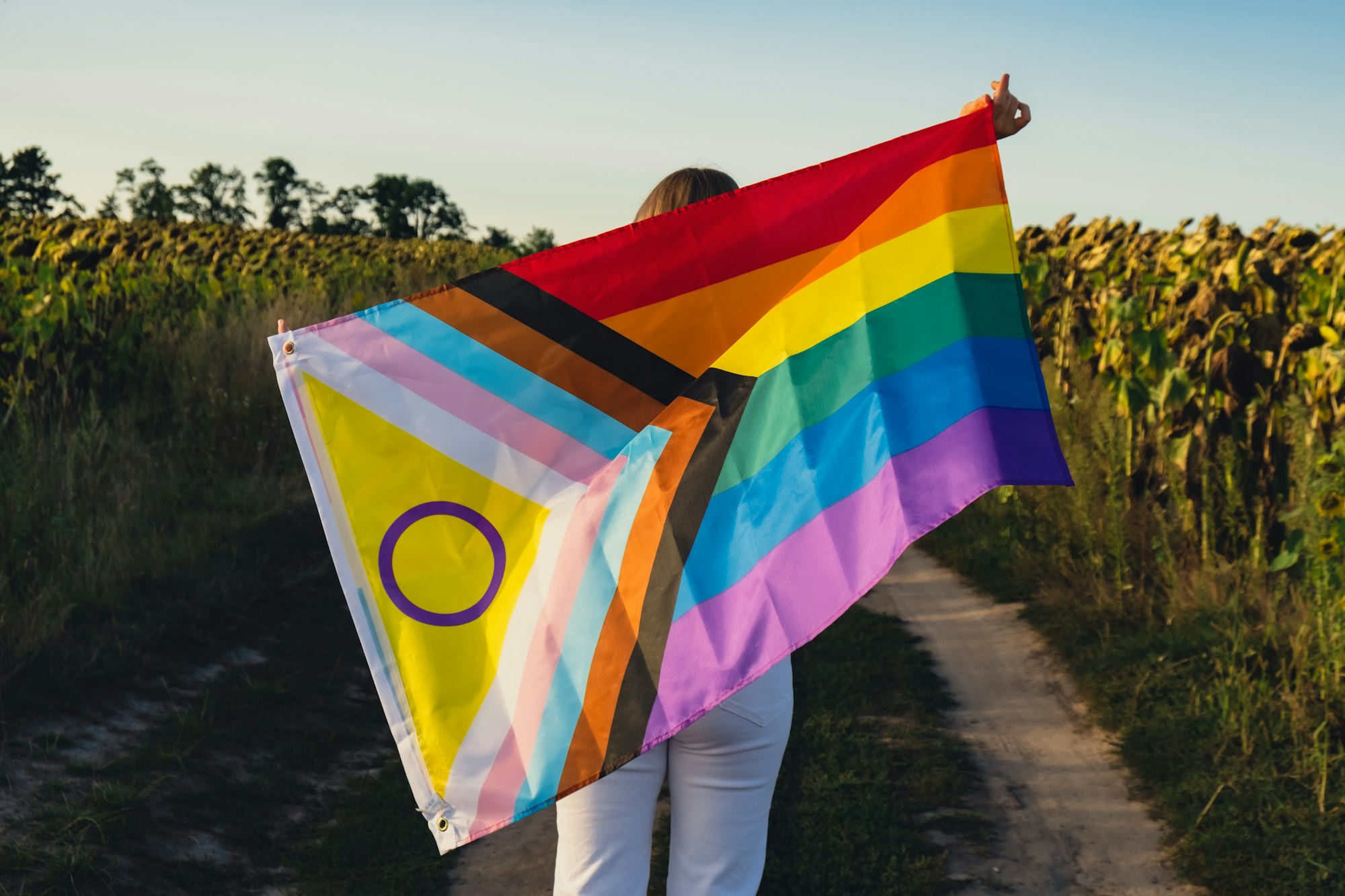 Young woman run in field with Rainbow LGBTQIA flag waving in wind made from silk material on field